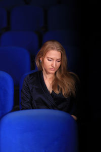 Sad young woman sitting on blue chair in darkroom