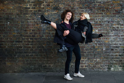 Happy boyfriend carrying girlfriend while standing against wall