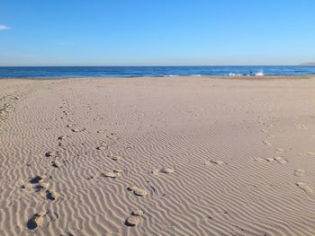 Footprints on sand at beach against clear blue sky