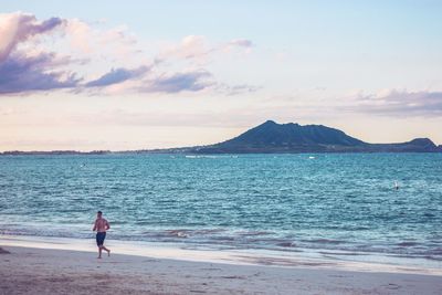 Rear view of man standing on beach against sky during sunset