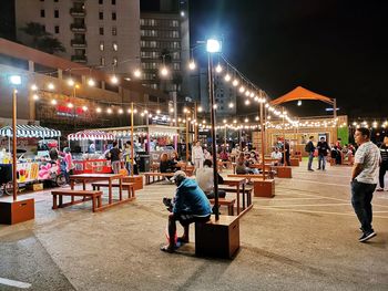Rear view of people walking on illuminated street at night
