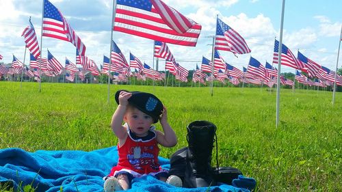 Portrait of cute baby boy wearing cap against american flags during us memorial day