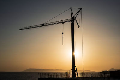 Silhouette cranes by sea against sky during sunset