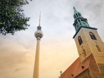 Low angle view of church and fernsehturm against cloudy sky