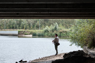 Side view of man standing and fishing on riverbank