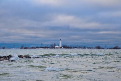 Lighthouse amidst sea and buildings against sky