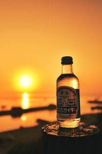 Close-up of bottle against orange sunset sky