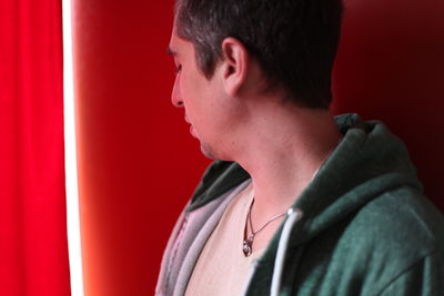 Close-up of thoughtful young man by red curtain