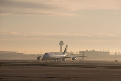 Airplane on airport runway against sky during sunset