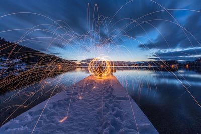 Light trails by sea against sky at night