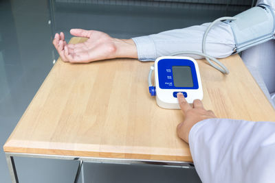 Cropped hand of doctor checking blood pressure of male patient at table