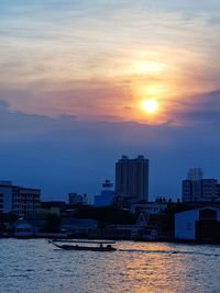 Sea by buildings against sky during sunset