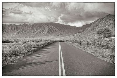 Road leading towards mountains against cloudy sky