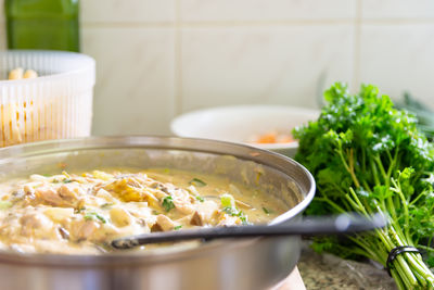 White sauce pasta dish in frying pan on chopping board with parsley, oil, spring onion and pasta