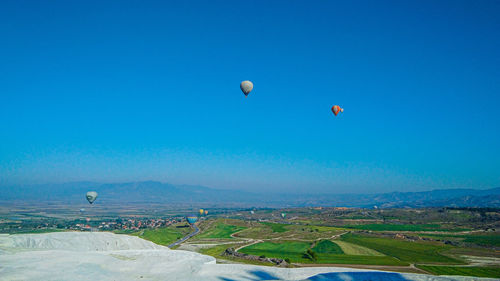 Hot air balloons flying over landscape against blue sky