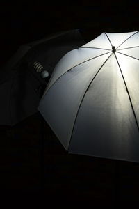 Low angle view of electric lamp behind umbrella against black background