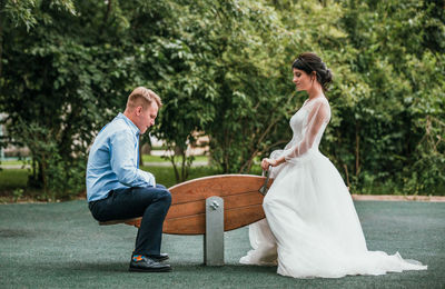 Rear view of couple sitting on sidewalk against trees