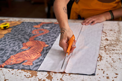 Anonymous adult female designer cutting fabric with scissors standing at workbench in studio