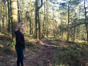 Side view of woman standing amidst trees in forest