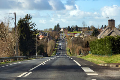 Empty road along trees and buildings against sky