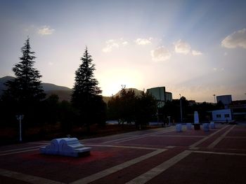 Empty road by buildings against sky during sunset