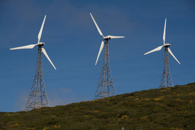 Low angle view of windmills against blue sky