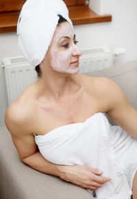 Woman with face mask sitting on sofa at home