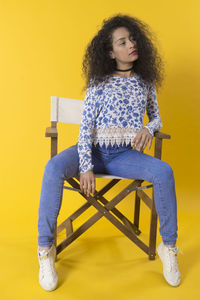 Young woman sitting on chair against yellow wall