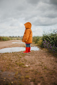 Rear view of boy standing on land against sky