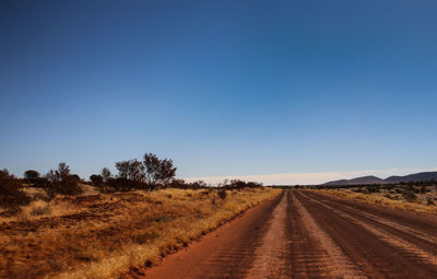 Road amidst field against clear blue sky