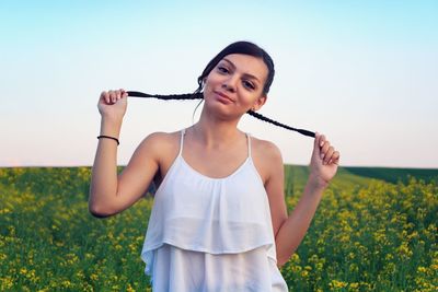 Young woman holding pig tails while standing on field against sky