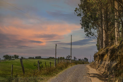 Road amidst field against sky during sunset