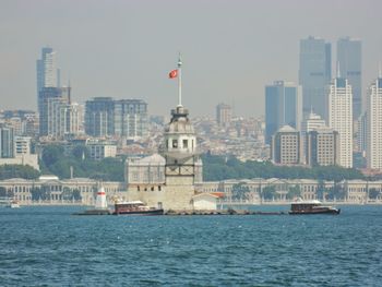 Sailboats in sea by buildings against sky in city