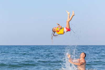 Strong man in sea tosses a 4-5 year girl. acrabatic trick against background of blue sky and sea