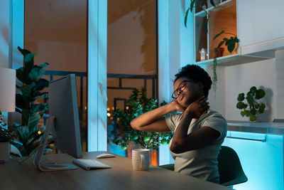 Young tired overworked multiracial woman freelancer in eyeglasses working late from home