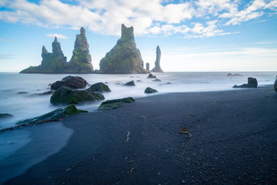 Long exposure of the coast of vik. rock formation in the sea close to the black volcanic beach.