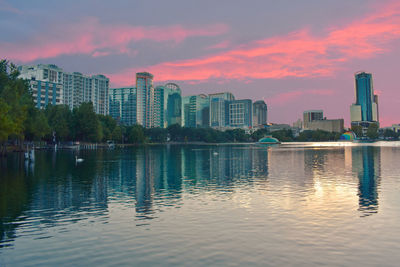 Scenic view of lake by buildings against sky during sunset