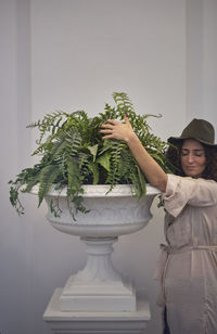 Woman holding plant in urn while standing against wall