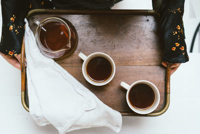 Cropped hands of woman holding coffee cups in tray on table