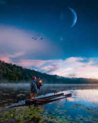 Young woman holding illuminated lantern while standing in boat on lake during sunset