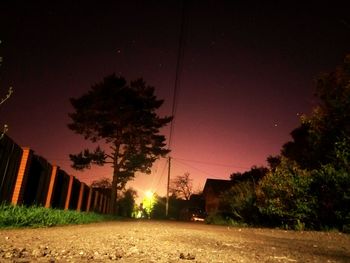 Silhouette trees by illuminated street against sky at night