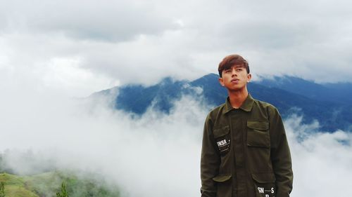 Portrait of young man standing on mountain against sky