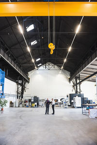 Two businessmen with clipboard on factory shop floor with bridge crane