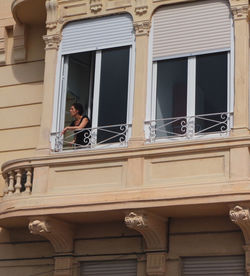 Low angle portrait of woman standing against window in building