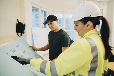 Female building contractor discussing over blueprint with male worker in office