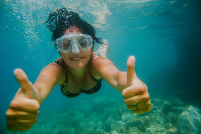 Portrait of woman swimming while gesturing thumbs up sign in sea