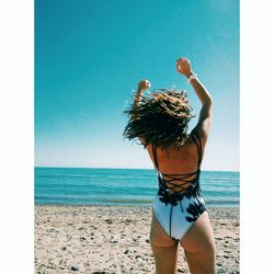 Rear view of woman standing at beach against clear sky