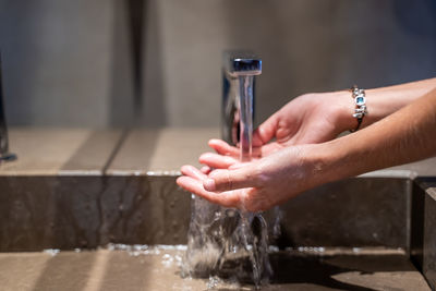 Midsection of person holding water from faucet