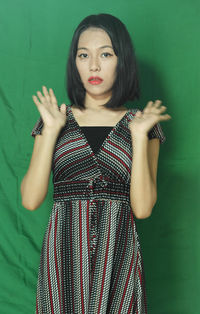 Portrait of beautiful young woman standing against green background