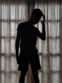 Silhouette man standing against window at home